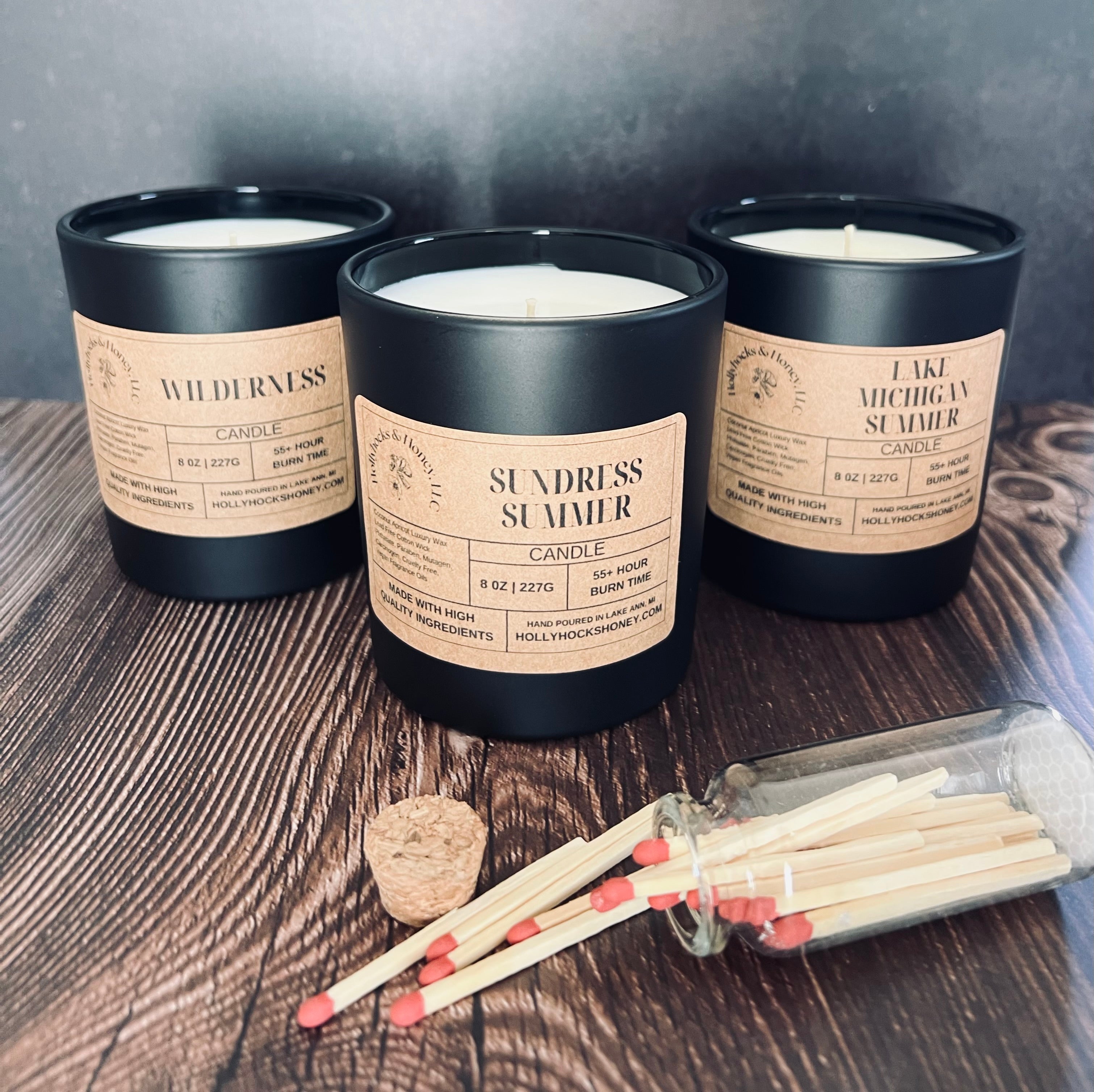 Three black candles with labels on a wooden surface, accompanied by matches.
