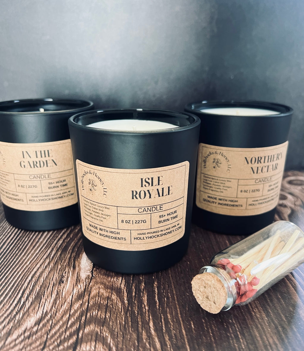 Three candles with labels on a wooden surface, accompanied by a bottle of matches.